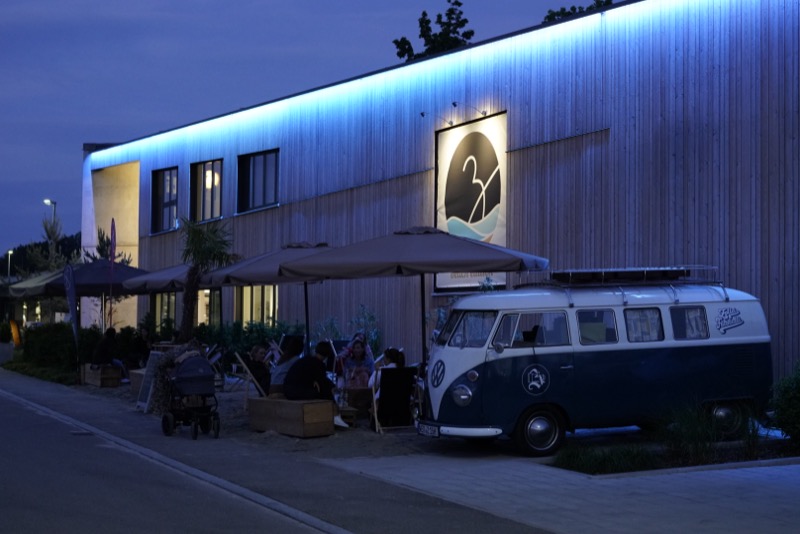 Bulli abends vor der Beach Edition Location, Gäste sitzen unter Sonnenschirmen