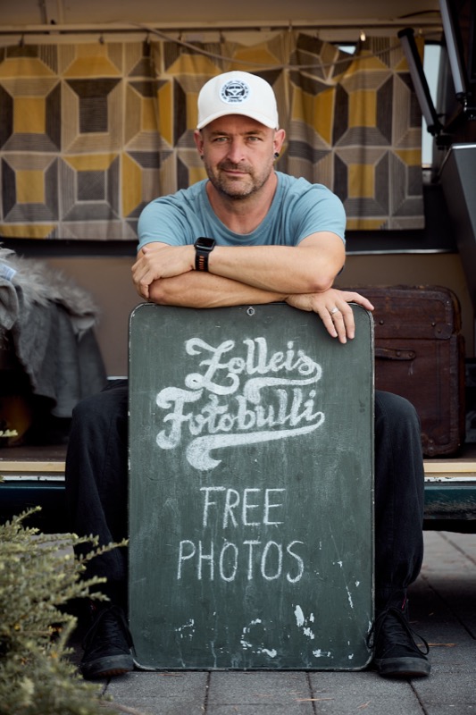 Jonas lehnt an der Zolleis Fotobulli Kreidetafel mit FREE PHOTOS Schriftzug